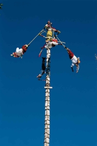 A group of traditional flying men at the top of a pole during a demonstration.