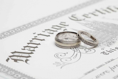 A male and female wedding ring on top of a marriage certificate.