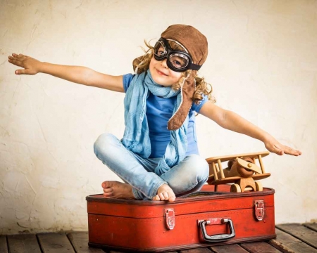 A little girl sitting on a suitcase pretending that she is flying.