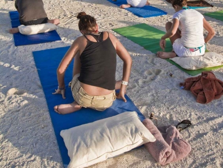 People doing yoga exercises on beach pads.
