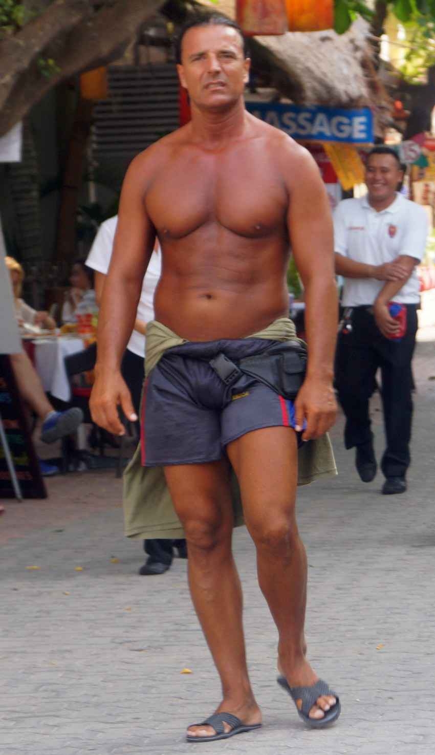 A darkly tanned and muscular man not wearing a shirt.
