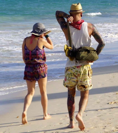 A man and a woman with a lot of tattoos walking on the beach.