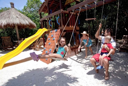 A mother and father with two children playing at a Playa Del Carmen family resort jungle gym.