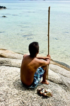 A young local boy was fishing with a fishing pole made from a stick.