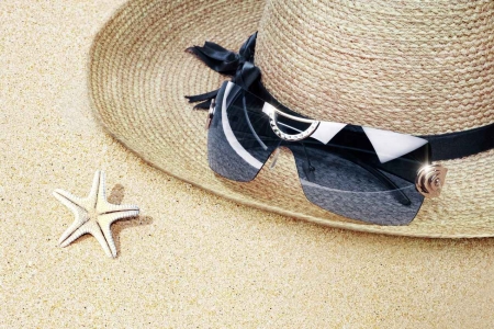 A sun hat with sunglasses on the sand.