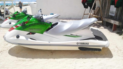 A side view of two green and white jet skis on the beach near the ferry dock in Playa Del Carmen.
