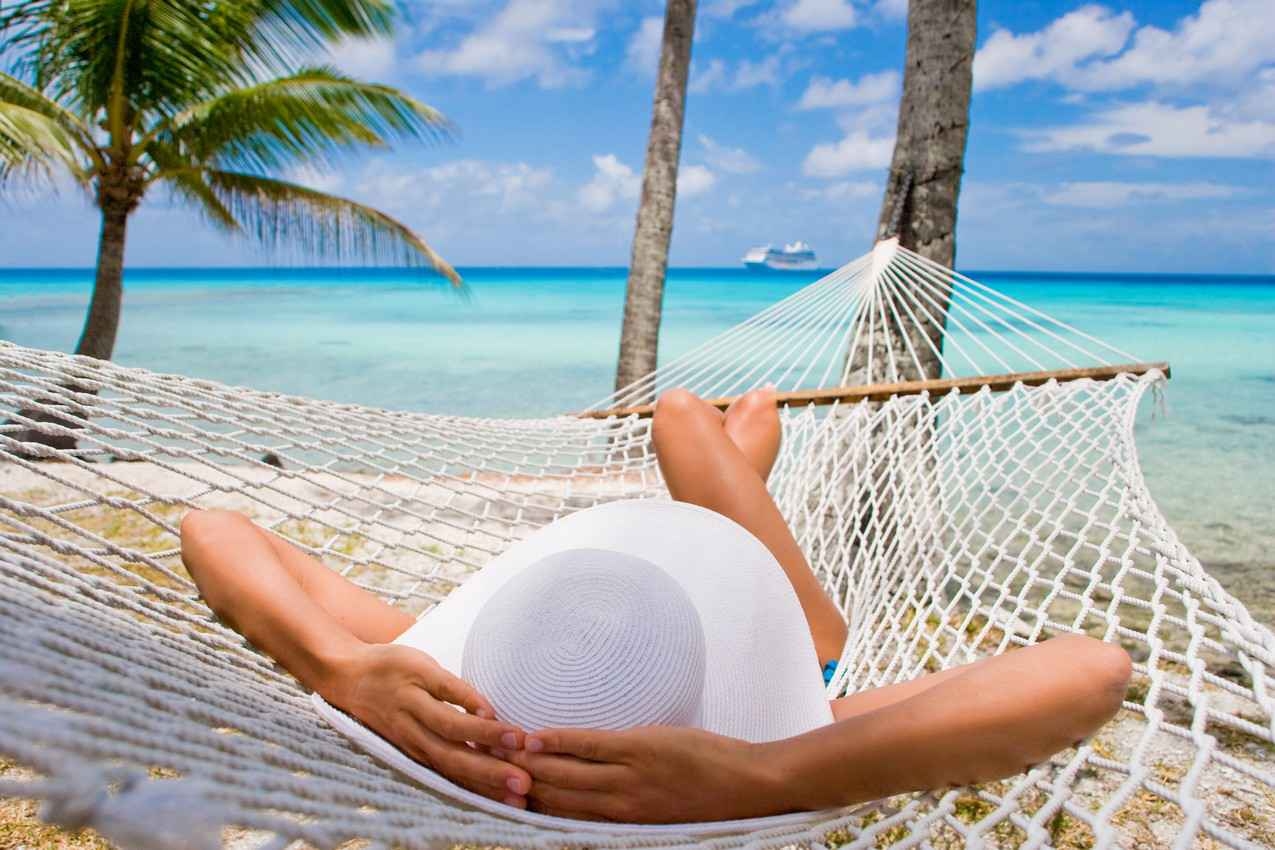 A woman comfortably lying in a hammock looking out at the Caribbean Sea.
