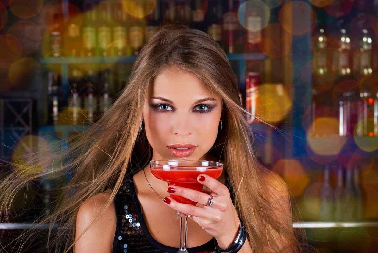 A super hot woman with nice makeup drinking a cocktail at a bar.