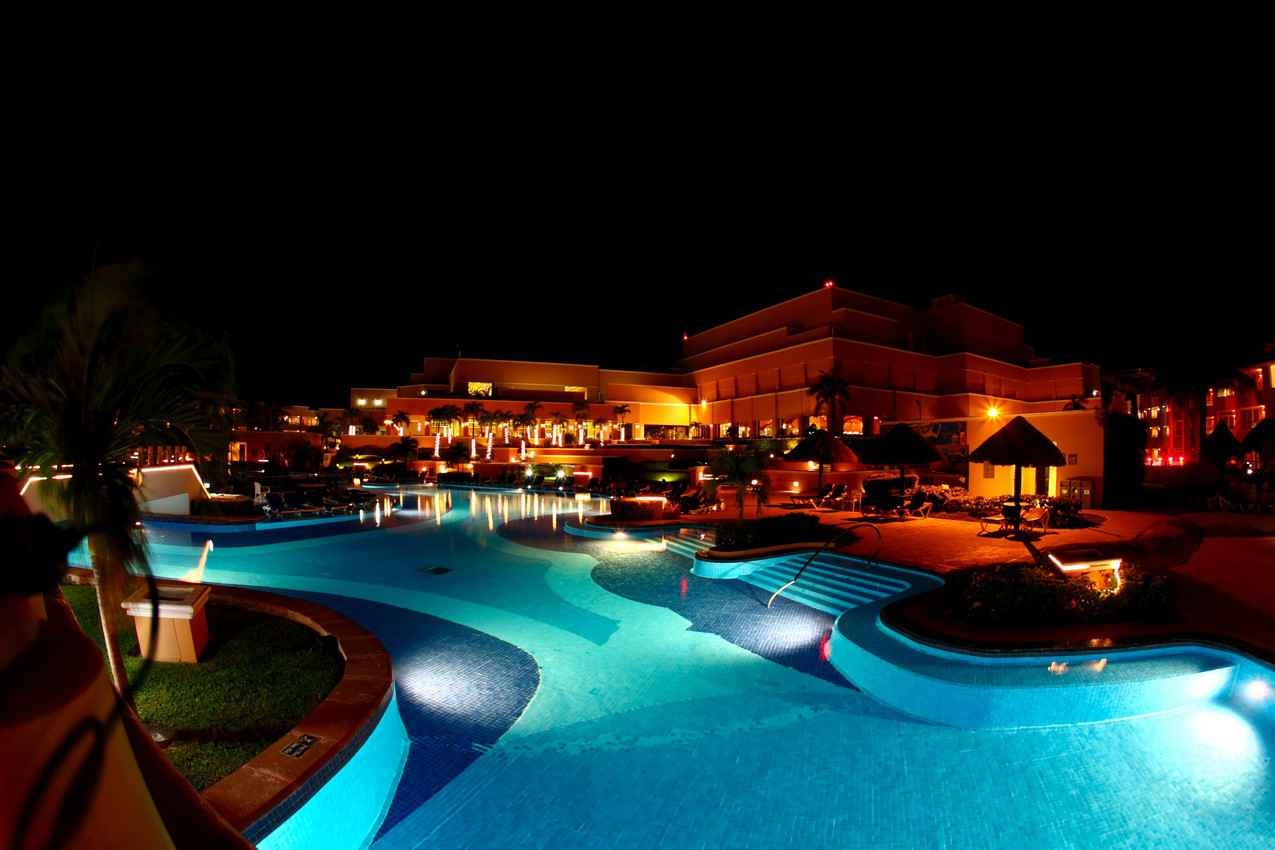 A beautiful and brightly lit resort swimming pool at night.