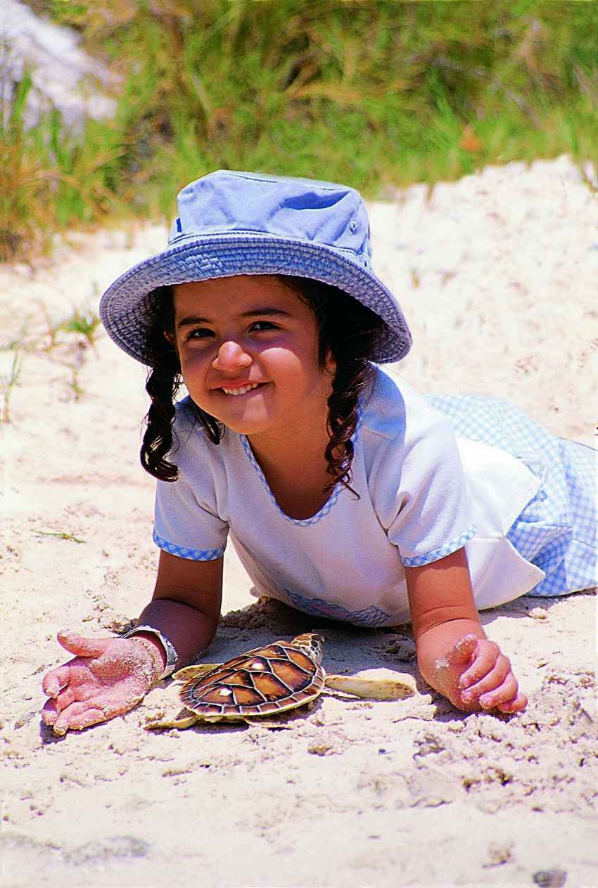 A young girl playing with a sea turtle on the beach.