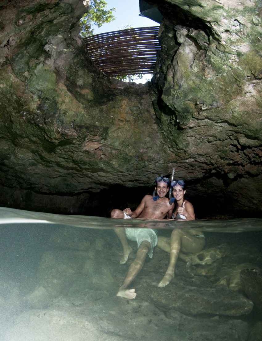 A man and a woman are sitting on rocks in an underground cenote.