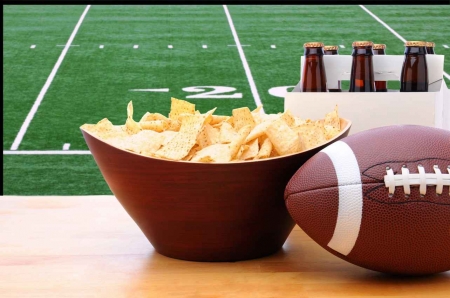 A football game playing in the background with tortilla chips and beer.