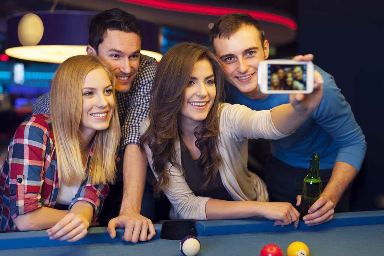 Two men and two women taking selfies at a sports bar.