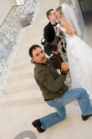 A wedding photographer taking a picture of a married couple on a large staircase.