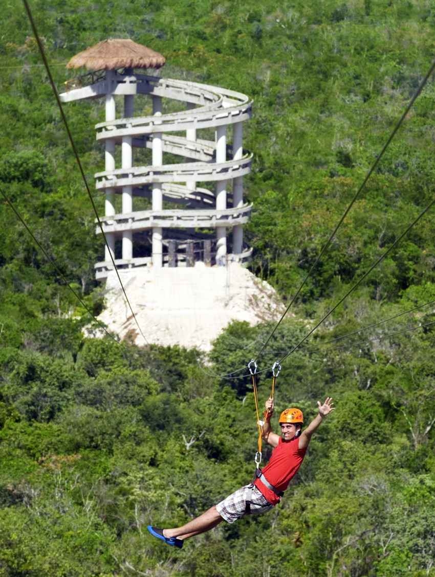 A person riding a zip line with a tower in the background.