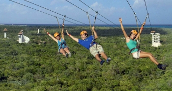 Three people hanging high above the jungle on a zip line.