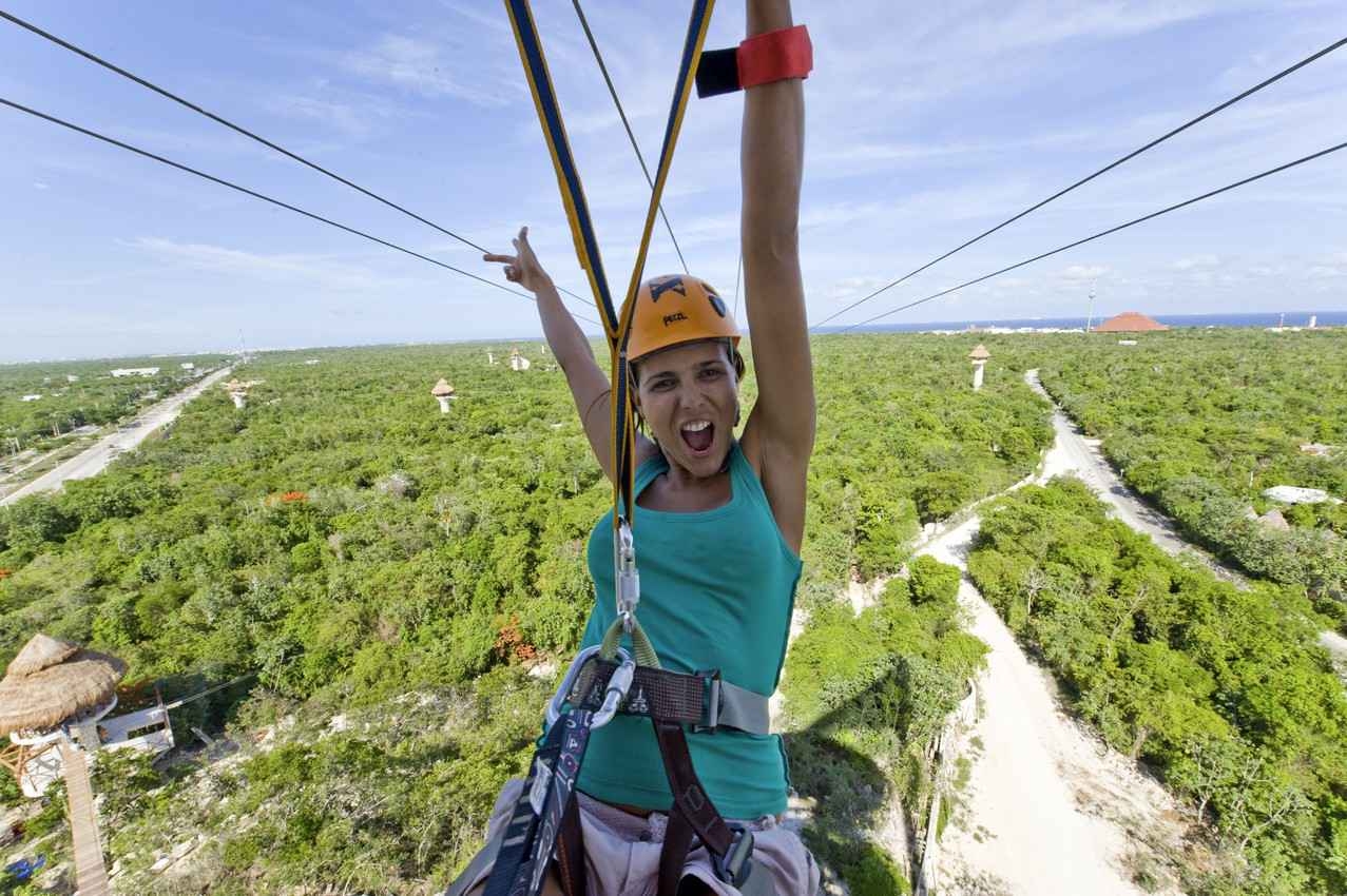A woman riding a zip line with several jungle trails visible below her.
