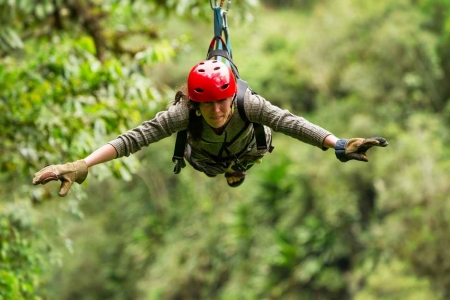 A woman with a red helmet riding a zip line in the jungle.