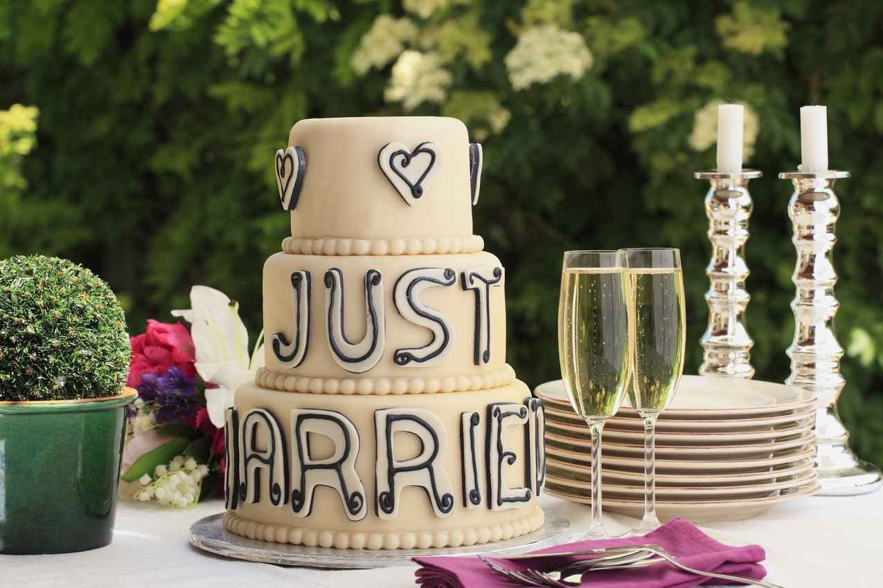 A wedding cake that says, JUST MARRIED, on it with champagne and serving utensils.