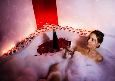 A woman enjoying a large glass of wine in a candlelit Jacuzzi.