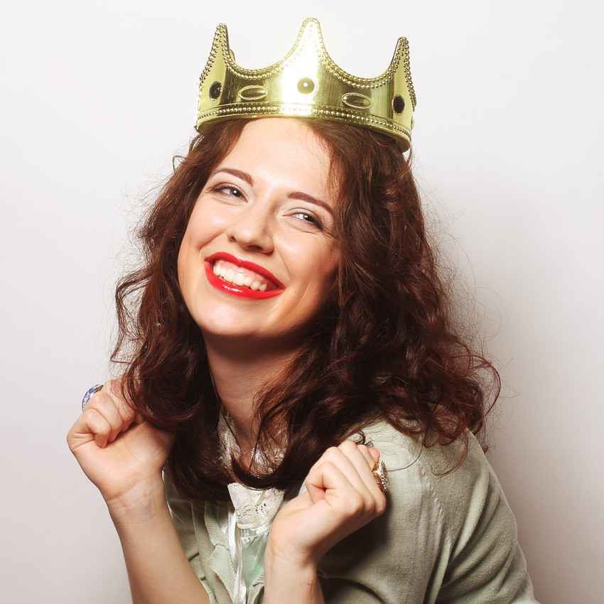 A crazy woman wearing a crown on her head and smiling ecstatically.