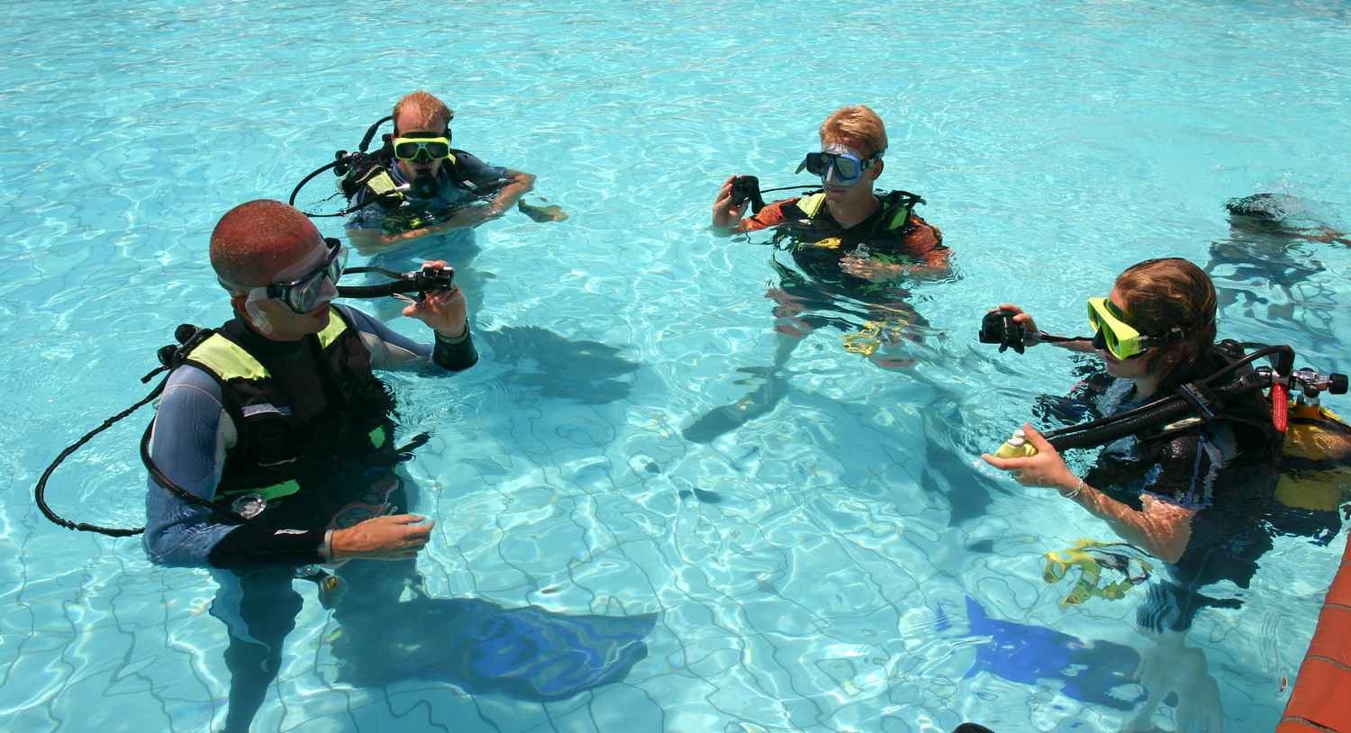 A scuba diving instructor working with three students in a swimming pool.