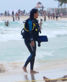 A woman on the beach in Playa Del Carmen who is wearing full scuba diving gear and walking out of the water.