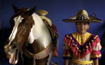 A Mexican horse rider standing near a horse with its mouth open.