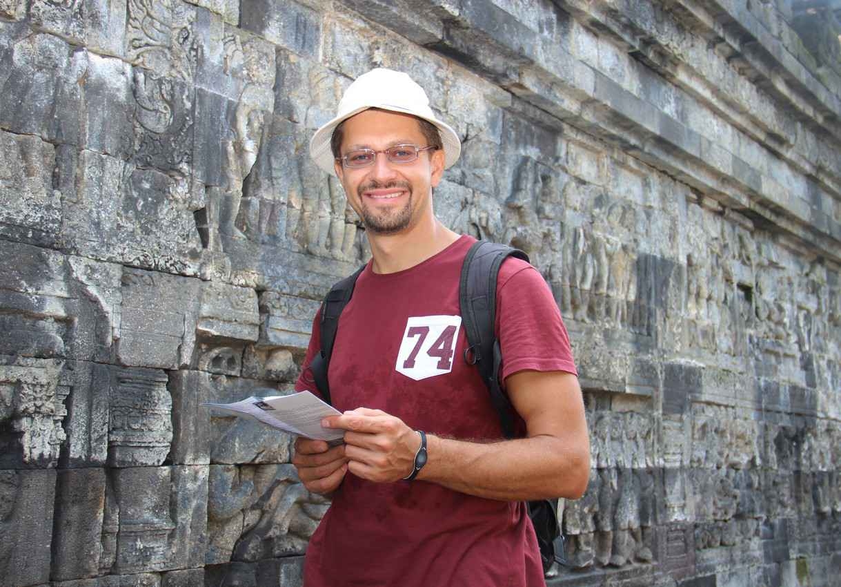 A student with a backpack looking at a tour map next to some Mayan ruins.