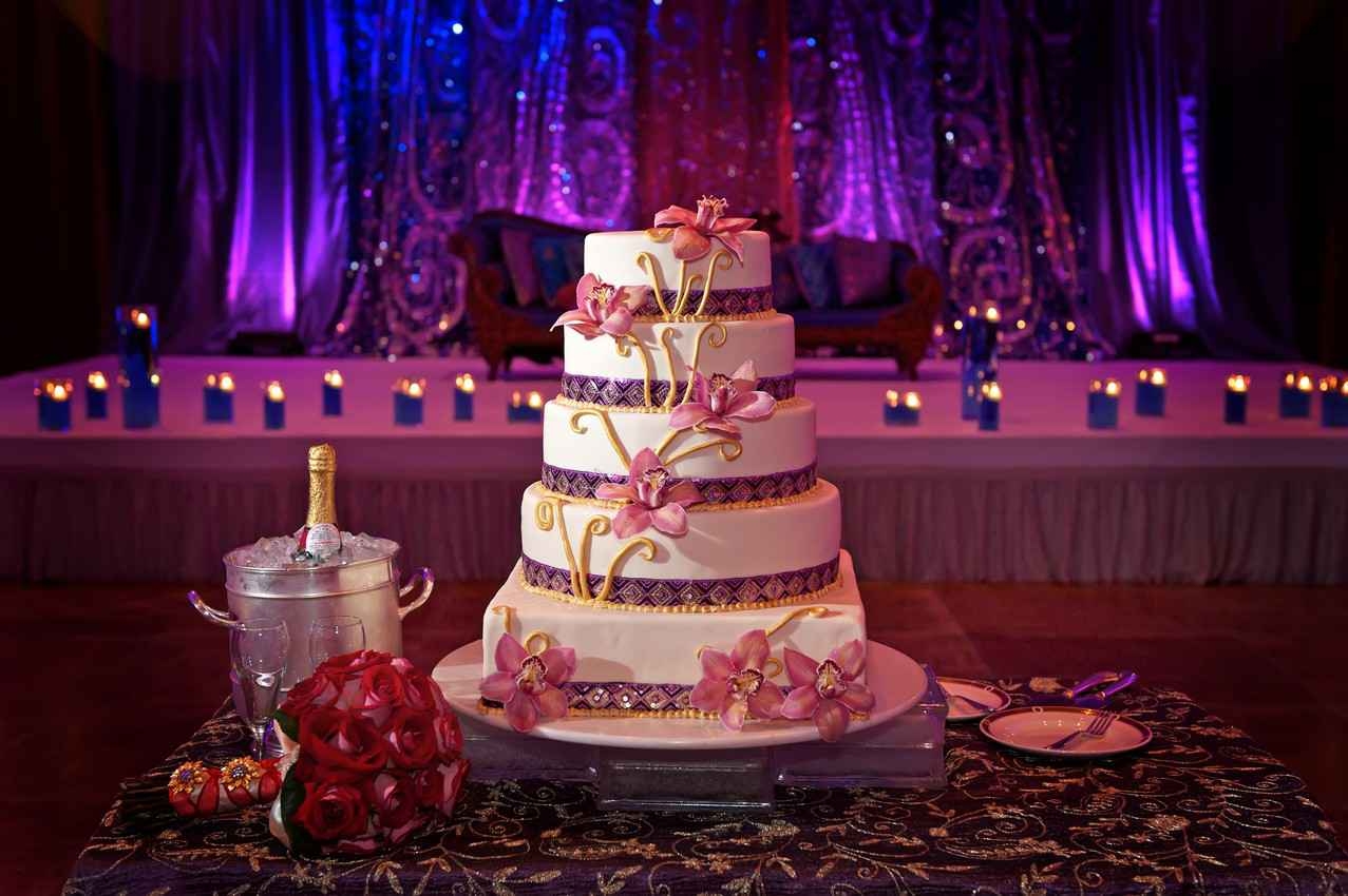 A wedding cake between several bottles of champagne and serving plates.