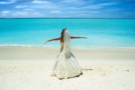 A bride standing on a beach with her arms outstretched.