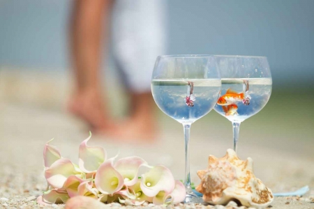 Two fish swimming together in two champagne glasses with a bride and groom visibly kissing in the reflection.