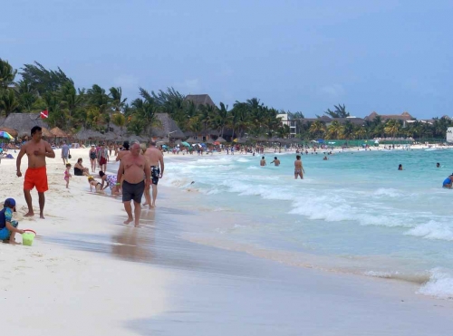 The Playa Del Carmen beach busy with people walking and swimming.