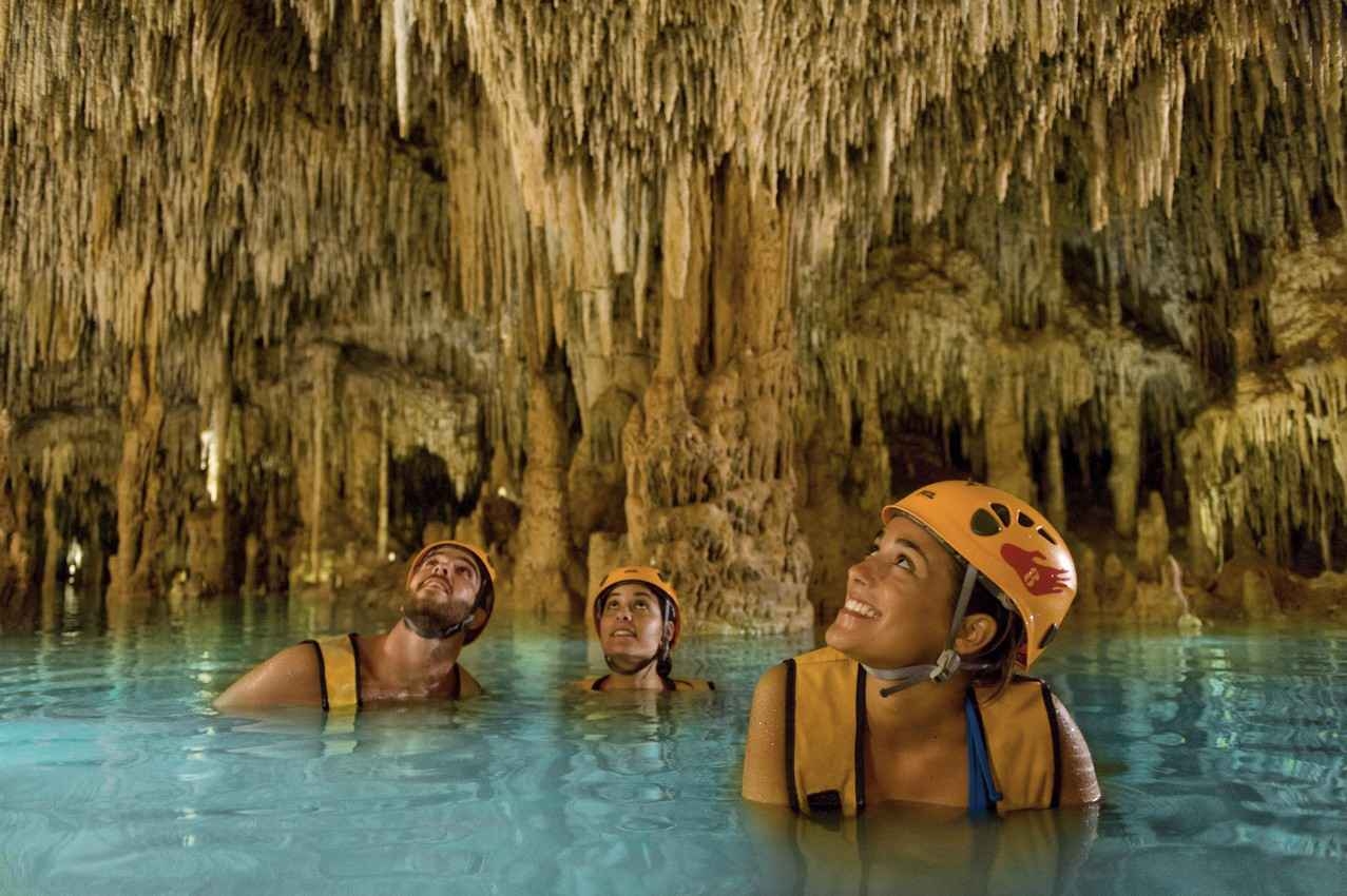 Several people with life jackets who are swimming in a large cenote.